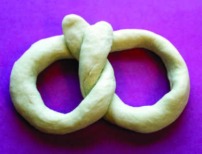 A raw, twisted pretzel on a red-pink work surface.